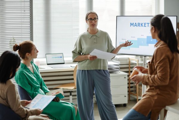 Young businesswoman with report standing at monitor with marketing graphs and performing for financial and tax experts.