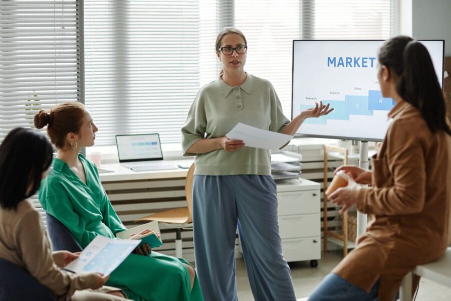 Young businesswoman with report standing at monitor with marketing graphs and performing for financial and tax experts.